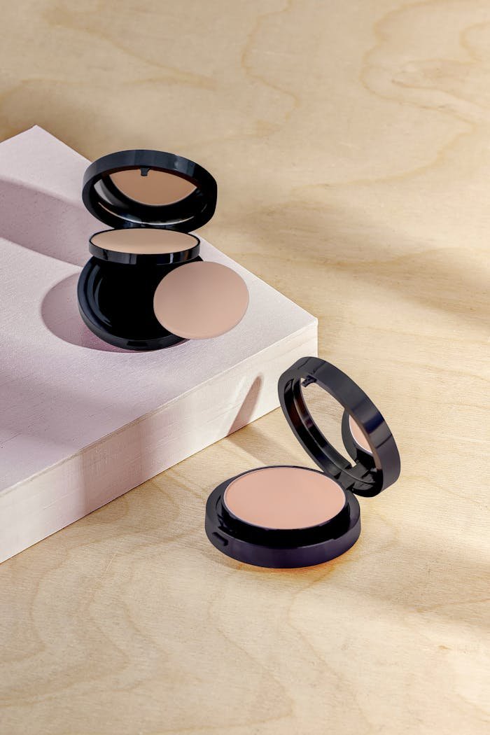 Open makeup compacts on a textured surface with soft lighting.